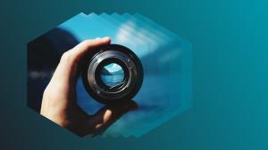 hand holding camera lens over layered hexagon graphic