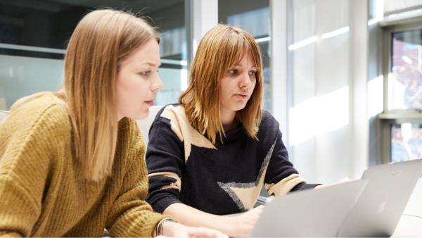 Two women with sitting next to each other reading a computer screen