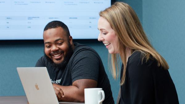 Two programmers seated, looking at one laptop screen