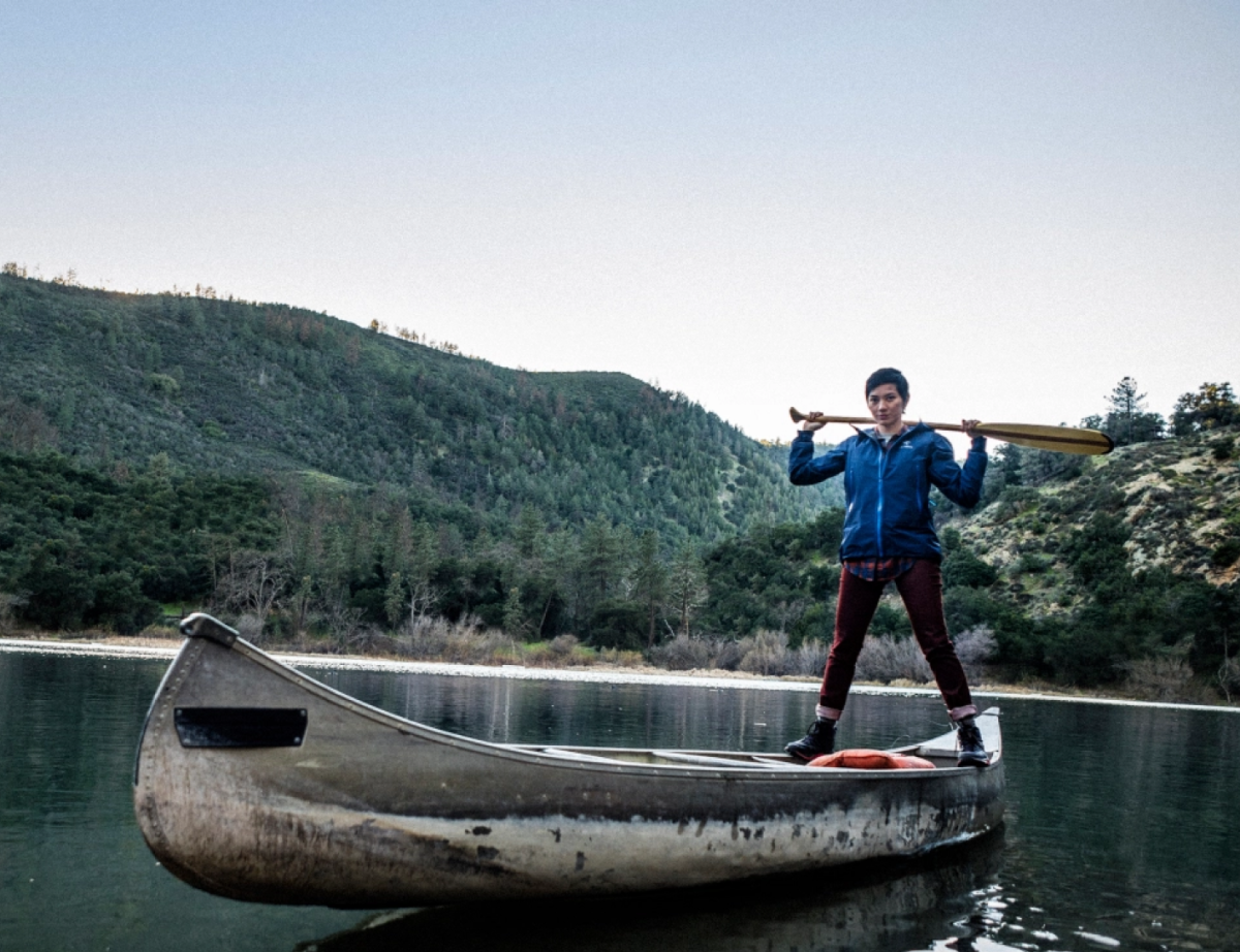 REI Canoe, woman holding an oar balancing on the edge of an aluminum canoe