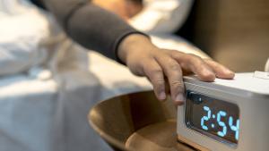 Digital alarm clock showing 2:54 in LED display, and a hand clicking the snooze button