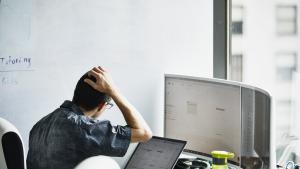 Person with hand on head looking at two monitors.