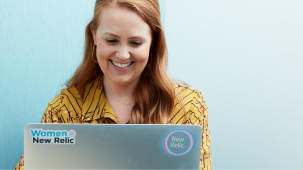 A New Relic teammate looking at a laptop: there is a Women at New Relic sticker and a New Relic logo sticker on the back of the laptop