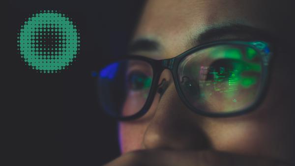 眼鏡をかけた人物とコンピュータ画面からの反射、緑の丸いグラフィック