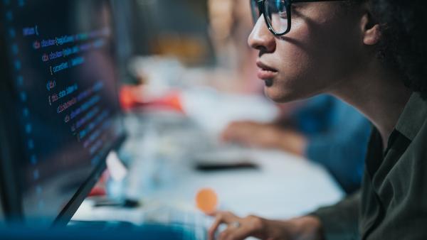 Focused black female programmer coding new computer language while working on desktop PC in the office.