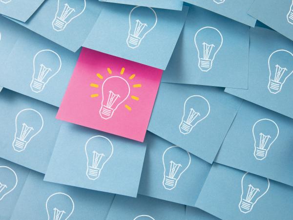 Conceptual iStock-1226583757.jpg four rows of cornflower blue post-it notes showing light bulbs, and one post-it note showing that is colored pink and the light bulb appears on