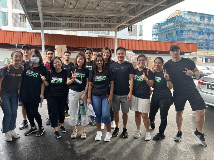 15 New Relic employees stand outside a local soup kitchen in Singapore, wearing New Relic Volunteer T-shirts and smiling